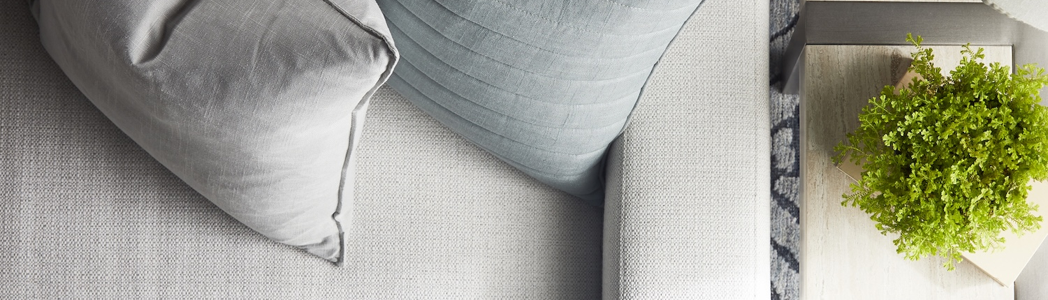 A gray sofa with two square pillows that can be customized through Traditions in Naples, FL or Minnesota.